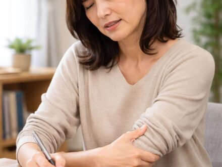 字を書いている最中に肘の後ろに痛みを感じ、肘を押さえている女性の様子